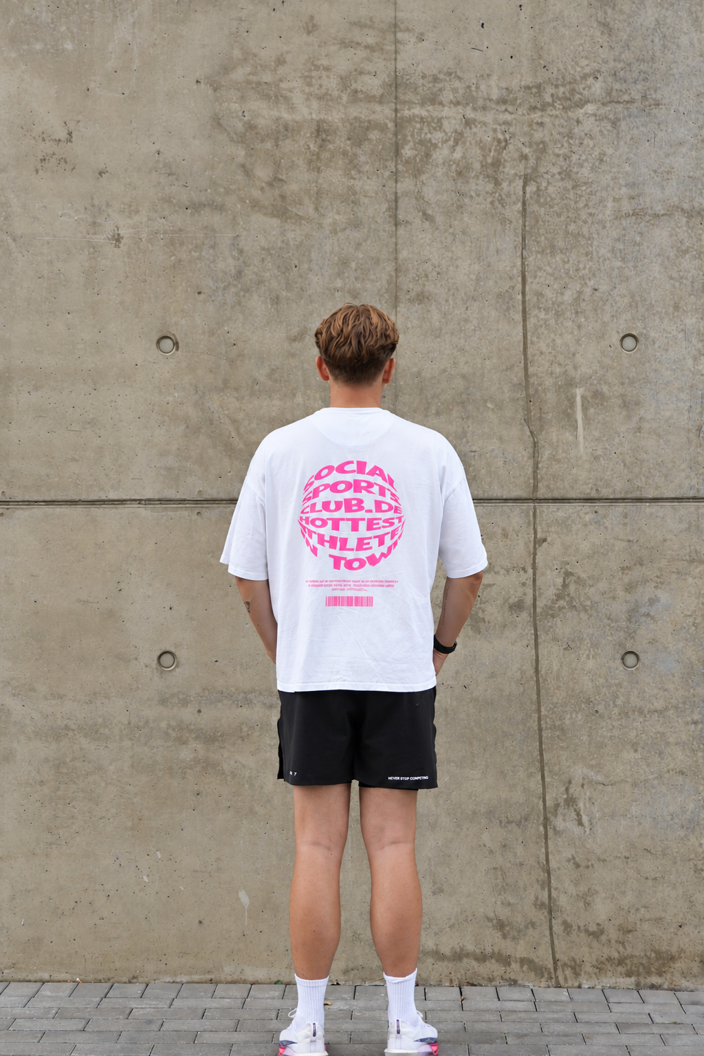 HOT-TEE 1.0 mit pinkem Backprint von hinten, getragen vor Betonwand – Social Sports Club